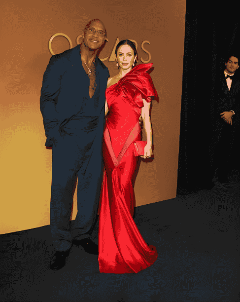 Breakdown of Dwayne Johnson’s Dark Teal Suit & Emily Blunt’s Red Sculptural Satin Gown